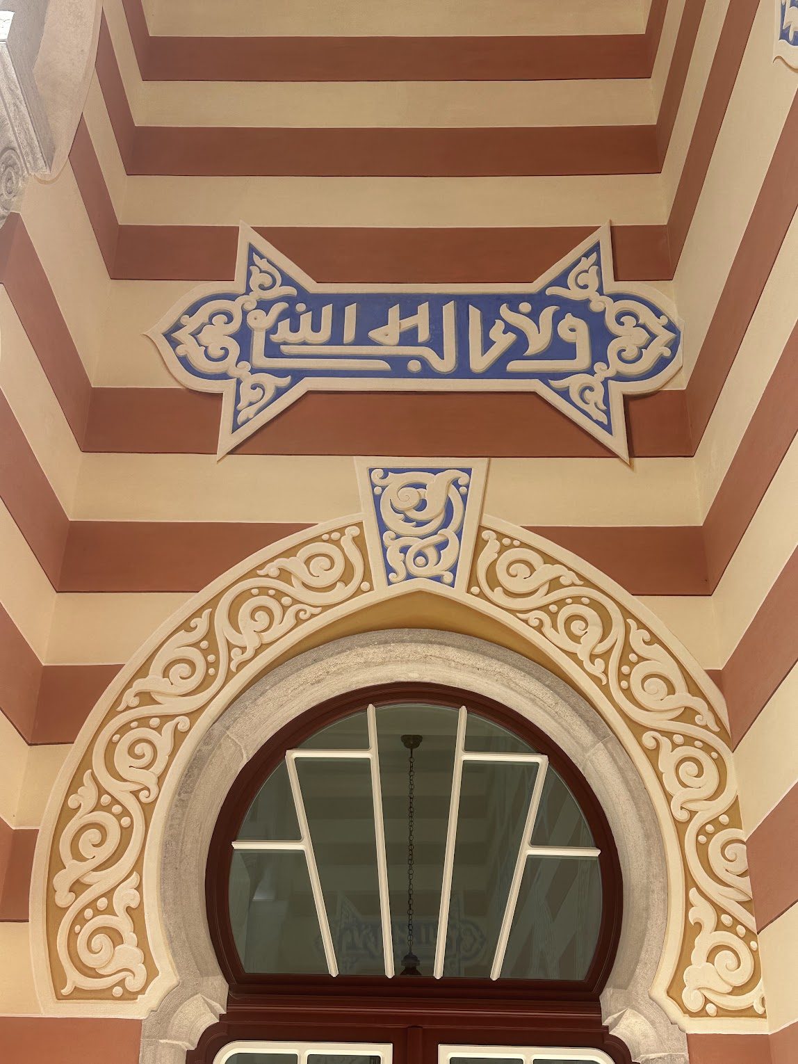 The Motto, Restored — White Kufic on Nasrid blue, three times repeated above the loggia doors.