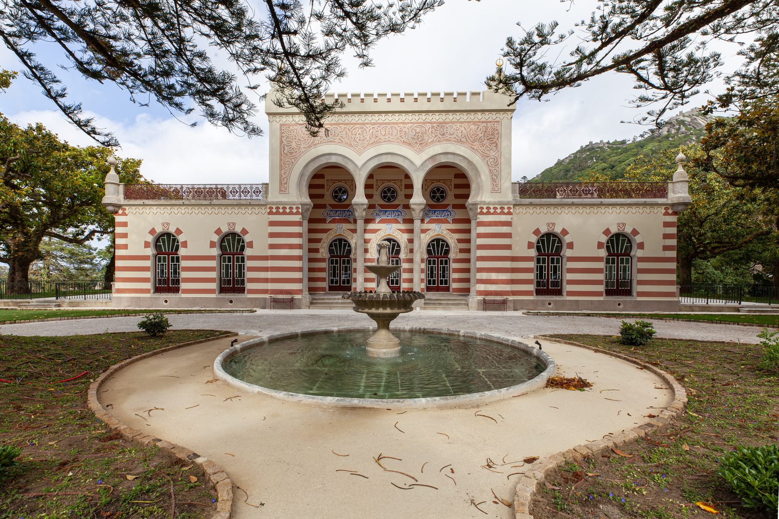 The Courtyard Fountain — The banded façade across the round basin — the view that greets you at the end of the garden walk.